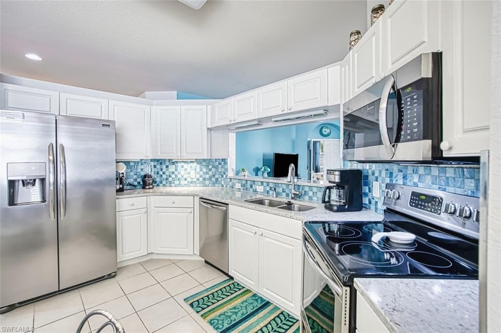 Kitchen with stainless steel appliances, light stone counters, light tile patterned floors, white cabinets, and backsplash