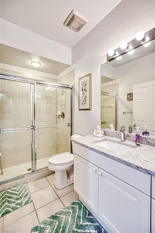 Full bath featuring vanity, light tile patterned flooring, a stall shower, and a textured wall