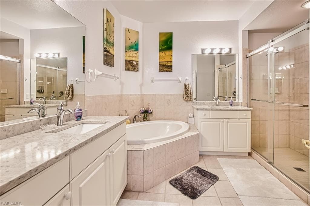 Full bathroom featuring a shower stall, a garden tub, two vanities, and light tile patterned floors