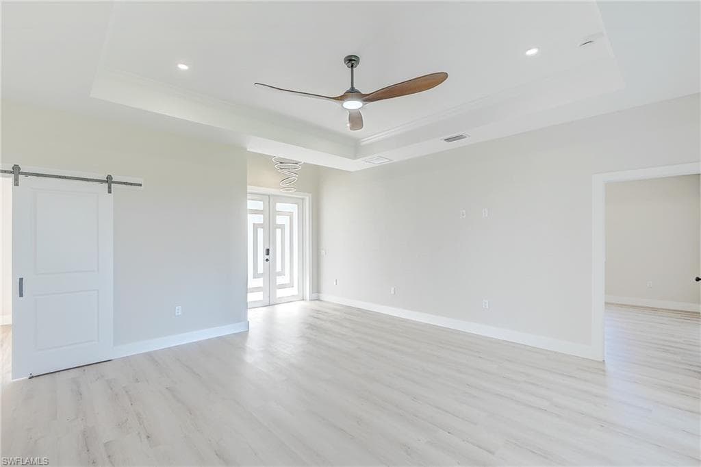 Empty room with a tray ceiling, french doors, light wood-type flooring, a ceiling fan, and recessed lighting