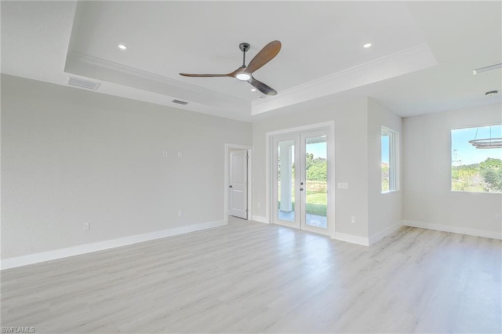 Kitchen with a raised ceiling, a kitchen bar, decorative light fixtures, light wood-style flooring, and white cabinets