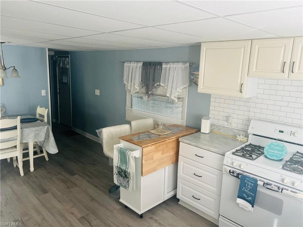 Kitchen with white range with gas cooktop, a paneled ceiling, tasteful backsplash, light countertops, and light wood finished floors
