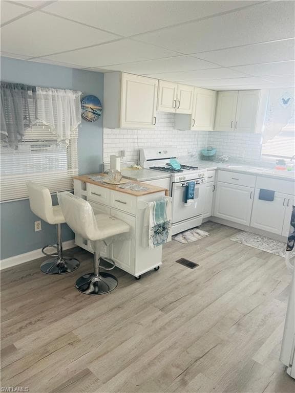 Kitchen with light countertops, white range with gas cooktop, white cabinetry, light wood-style flooring, and backsplash
