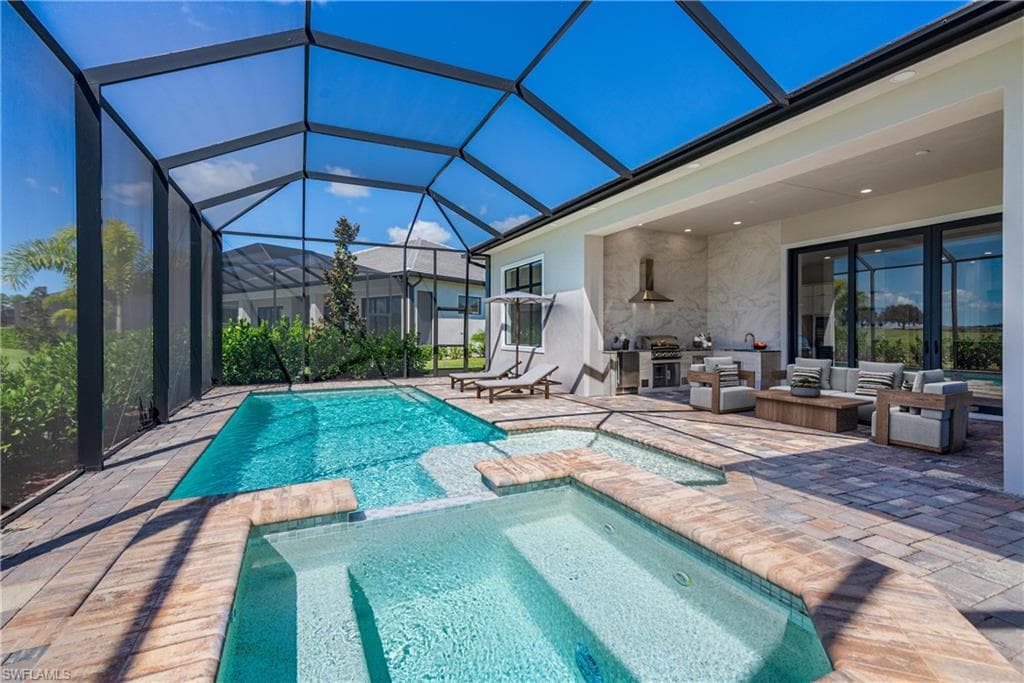 View of pool featuring a pool with connected hot tub, a patio, a sunroom, and glass enclosure