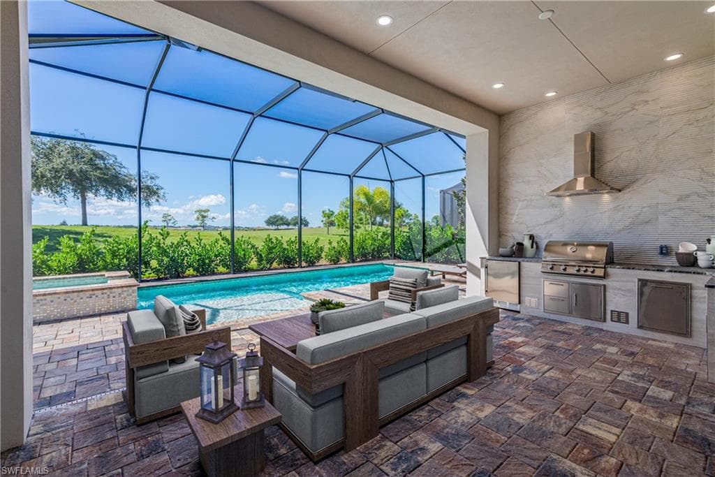 View of patio featuring a lanai, a sunroom, exterior kitchen, and a pool with connected hot tub