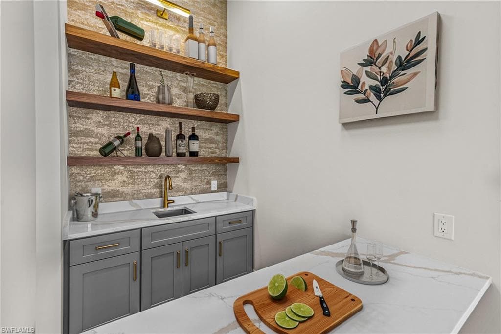 Indoor wet bar featuring gray cabinetry, light stone countertops, decorative backsplash, and open shelves