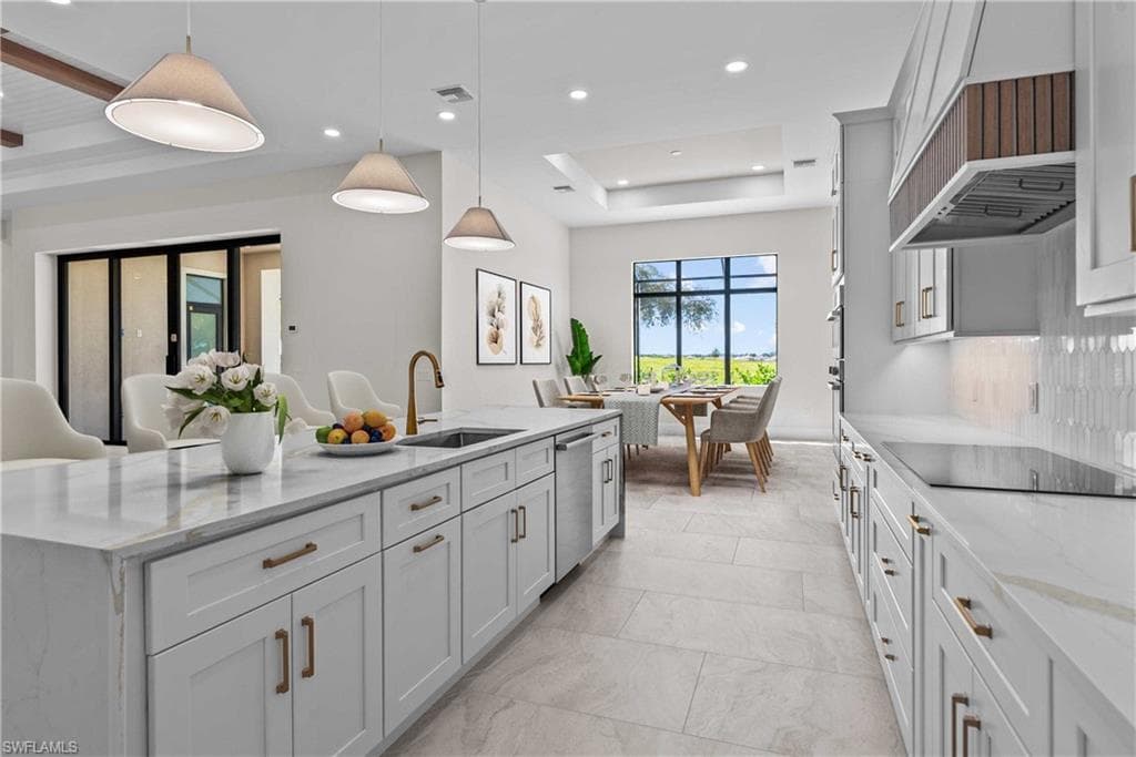 Kitchen featuring a tray ceiling, light stone counters, hanging light fixtures, white cabinets, and recessed lighting