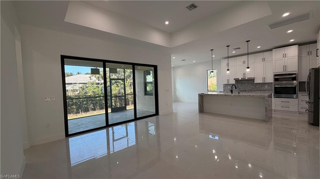 Kitchen with light stone counters, a kitchen island with sink, appliances with stainless steel finishes, pendant lighting, and white cabinetry