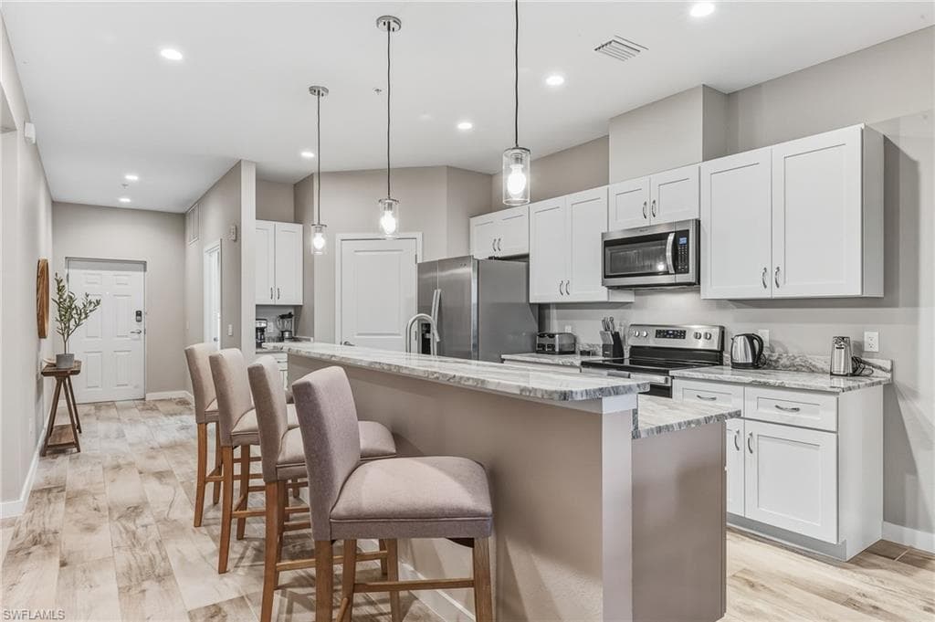 Kitchen with light wood-style flooring, a breakfast bar area, stainless steel appliances, hanging light fixtures, and a center island with sink