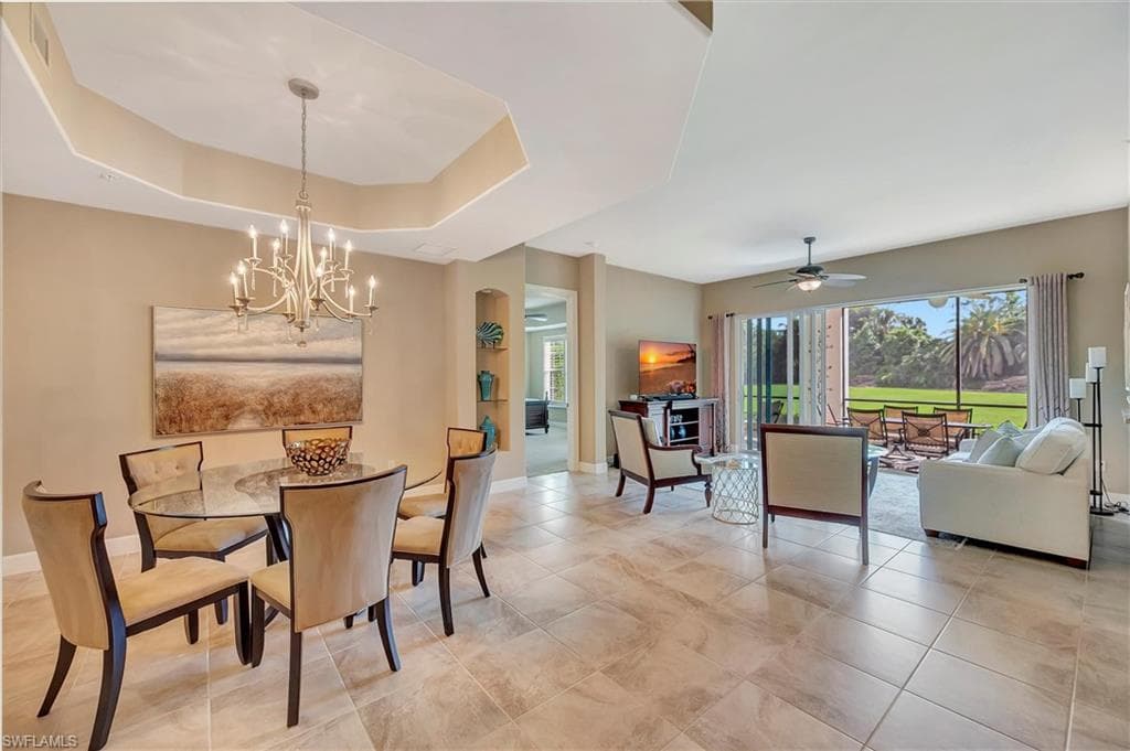 Dining area with a tray ceiling, a ceiling fan, a chandelier, and light tile patterned floors
