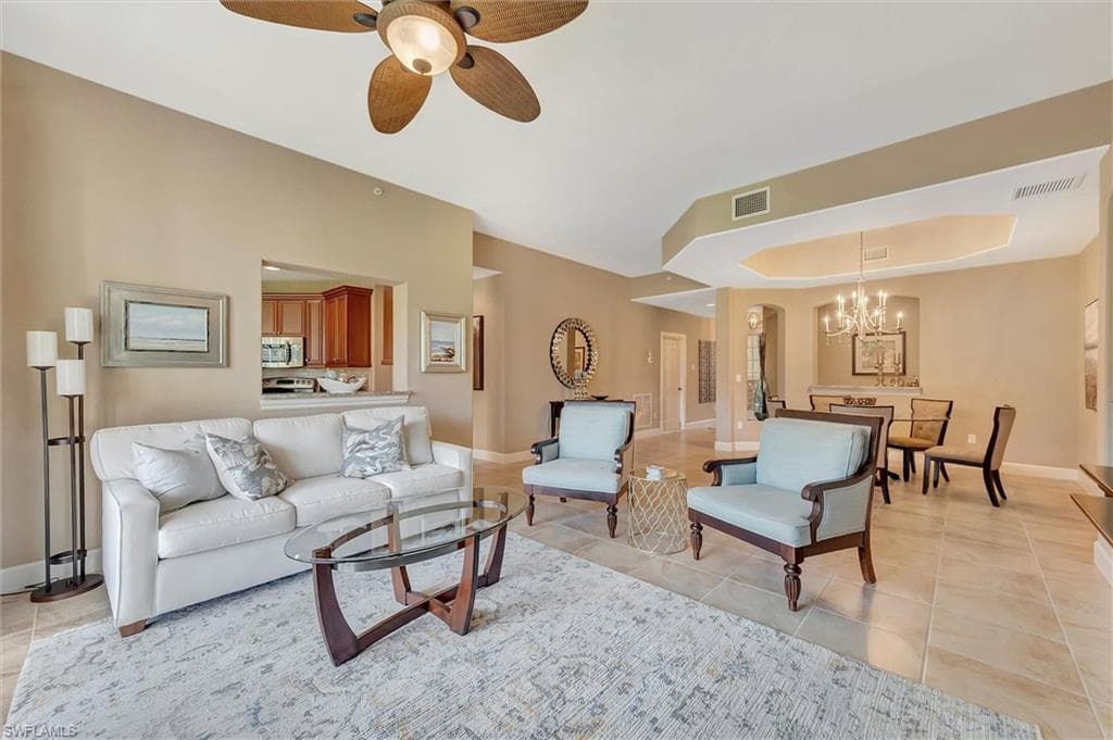 Living room with a raised ceiling, light tile patterned flooring, a chandelier, and ceiling fan