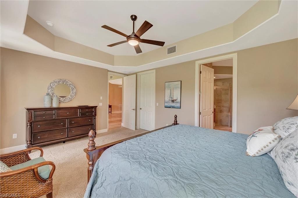 Carpeted bedroom featuring a tray ceiling, a ceiling fan, and connected bathroom