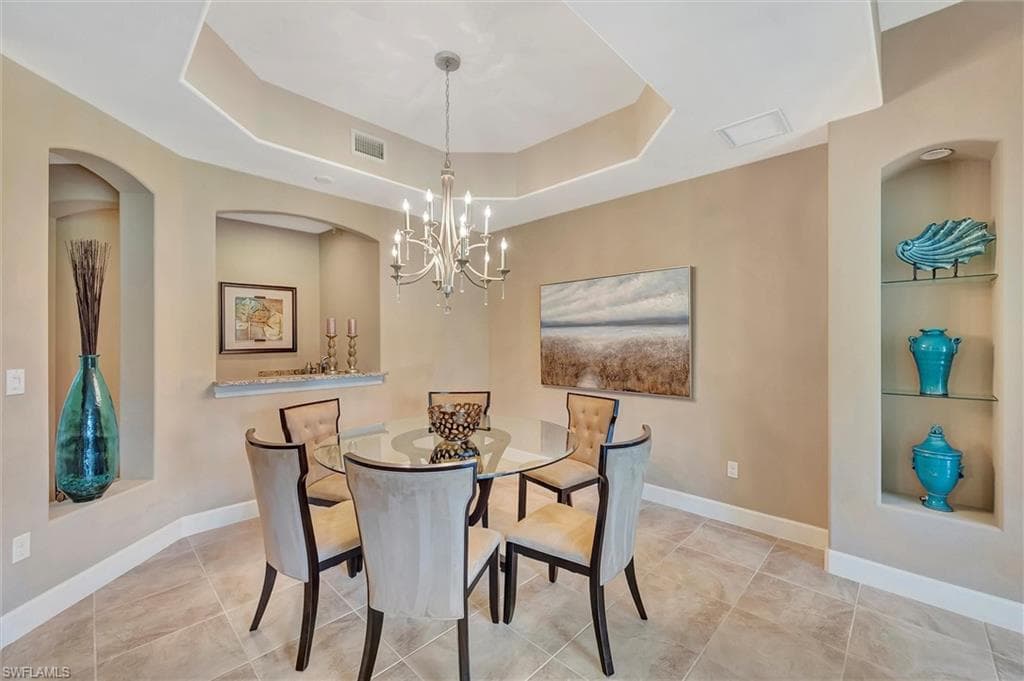 Dining space featuring a tray ceiling, a chandelier, built in shelves, arched walkways, and light tile patterned floors