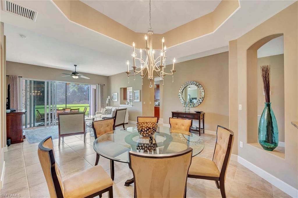 Dining area with a raised ceiling, a ceiling fan, tile patterned floors, a chandelier, and arched walkways