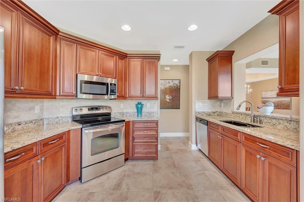 Kitchen featuring appliances with stainless steel finishes, tasteful backsplash, light stone countertops, brown cabinets, and recessed lighting