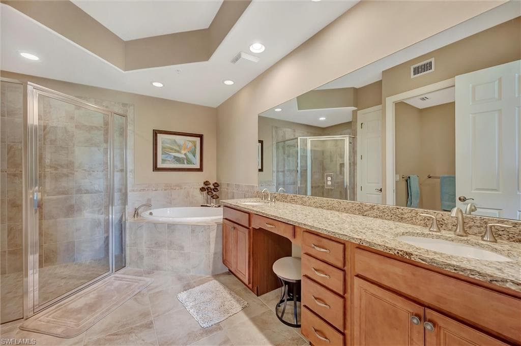 Bathroom featuring a garden tub, double vanity, a shower stall, and light tile patterned flooring