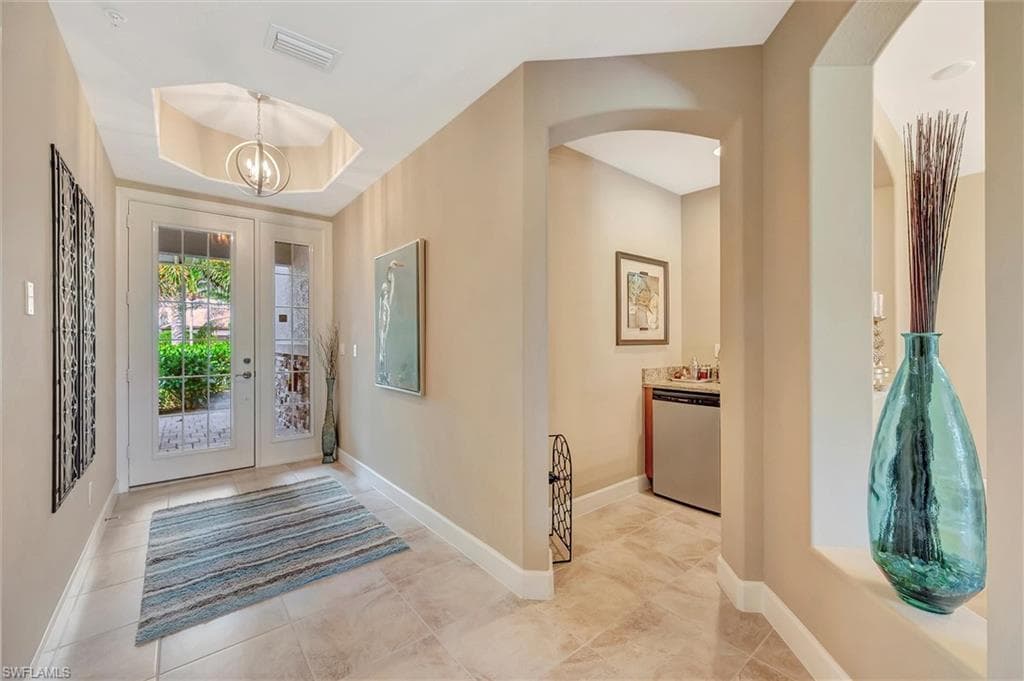 Entrance foyer with a tray ceiling, a chandelier, and light tile patterned flooring