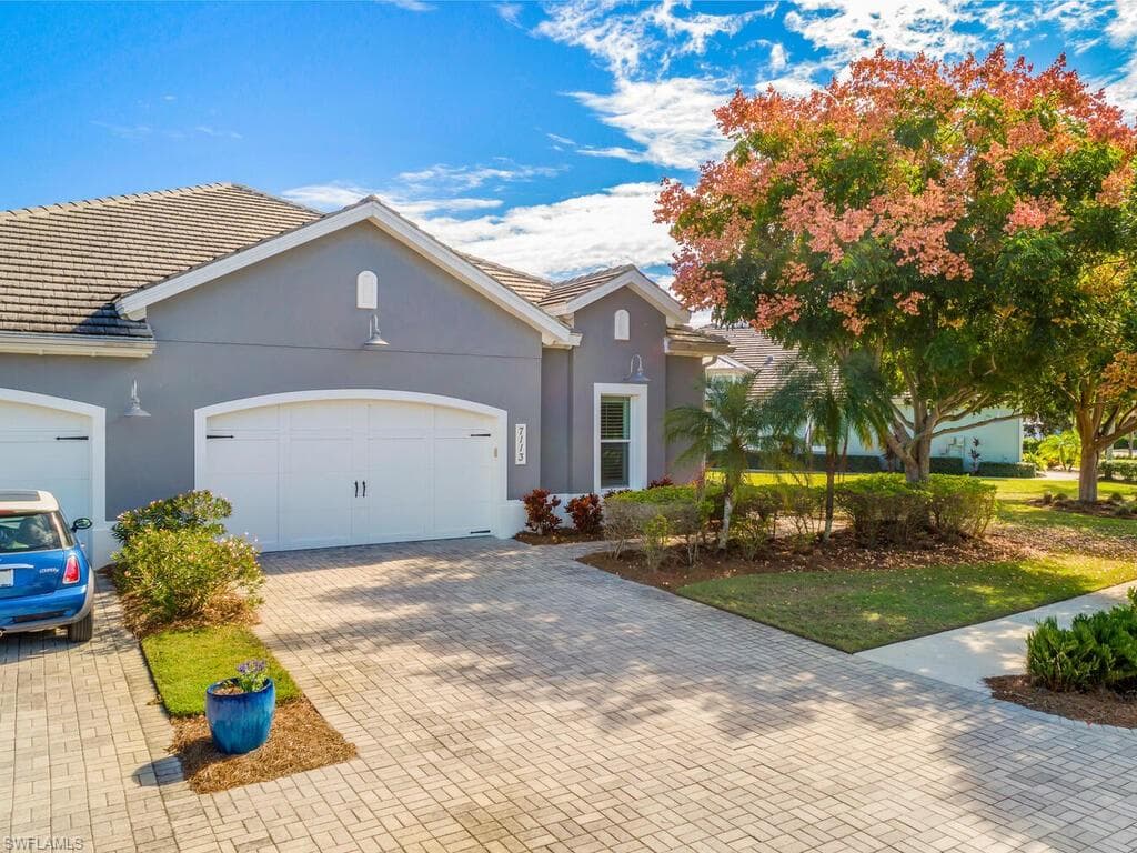 Coastal-style home with a tiled roof, brick paver driveway, stucco siding, and an attached 2 Car garage