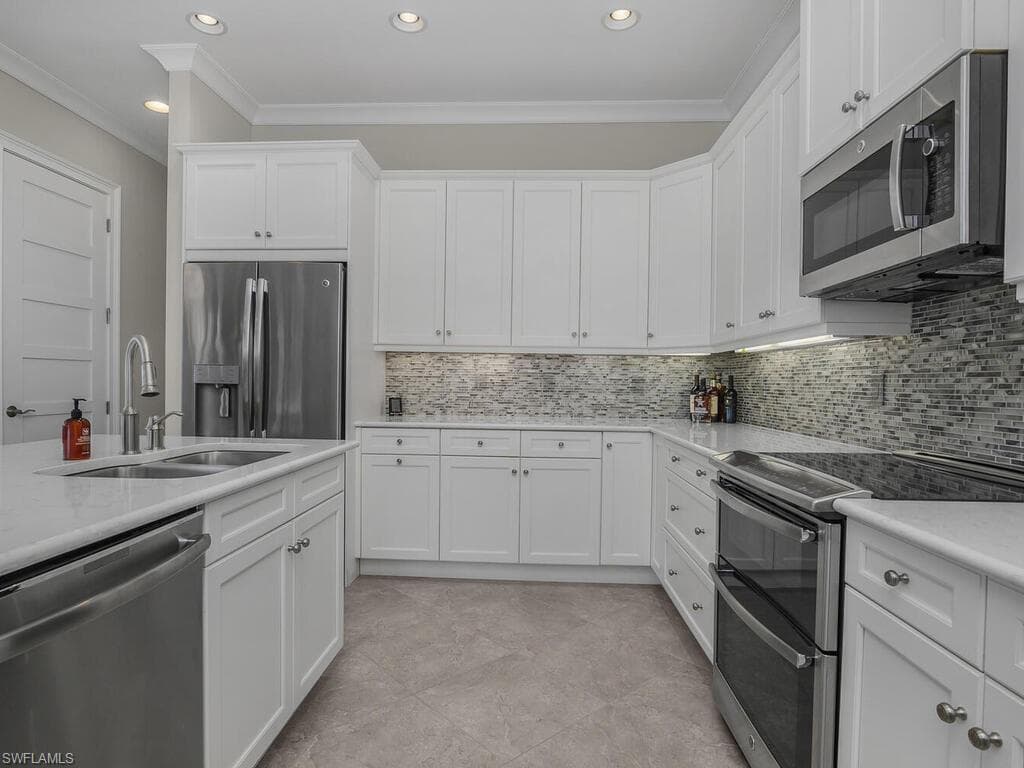 Kitchen with stainless steel appliances, ornamental molding, white cabinets, tasteful backsplash, and recessed lighting. Quartz counter tops.
