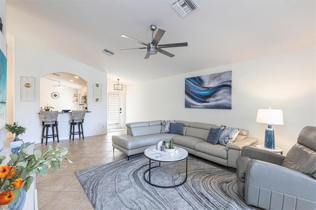 Tiled living room with a ceiling fan, arched walkways, and lofted ceiling