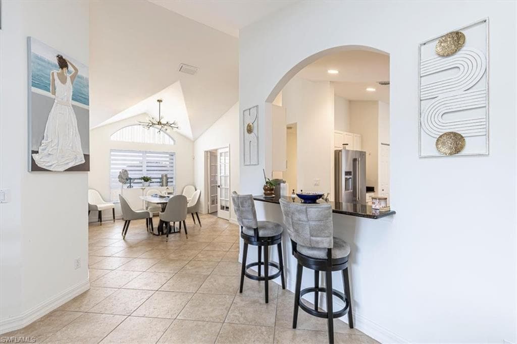 Kitchen with a breakfast bar area, high vaulted ceiling, dark countertops, high quality fridge, and arched walkways