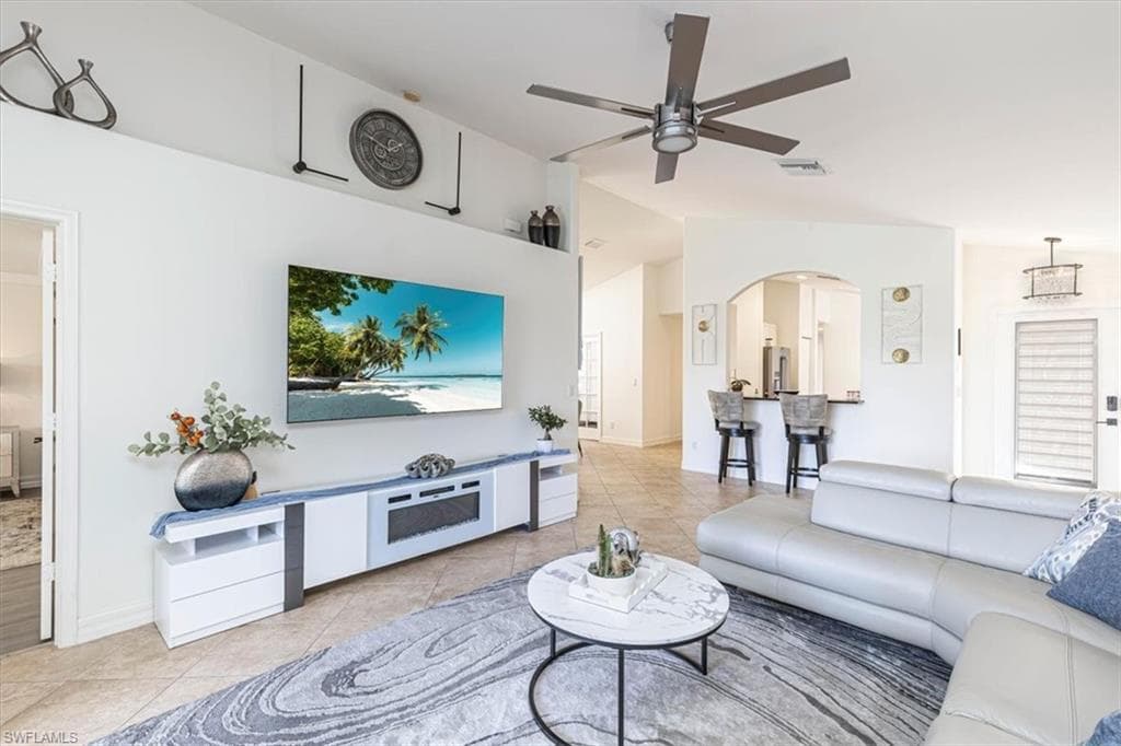 Living room featuring light tile patterned floors, lofted ceiling, ceiling fan, and arched walkways