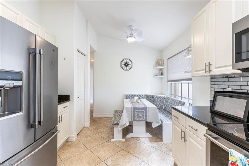 Kitchen with appliances with stainless steel finishes, light tile patterned floors, dark stone countertops, and white cabinetry