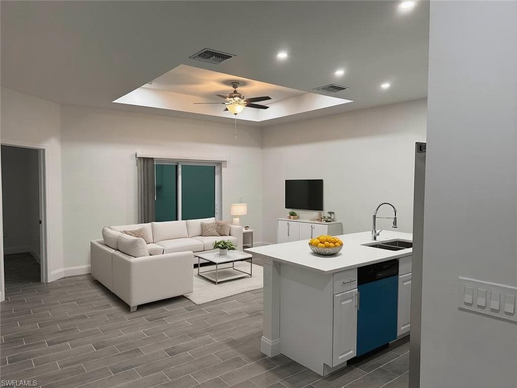 Kitchen featuring a tray ceiling, open floor plan, dishwashing machine, wood finish floors, and a peninsula
