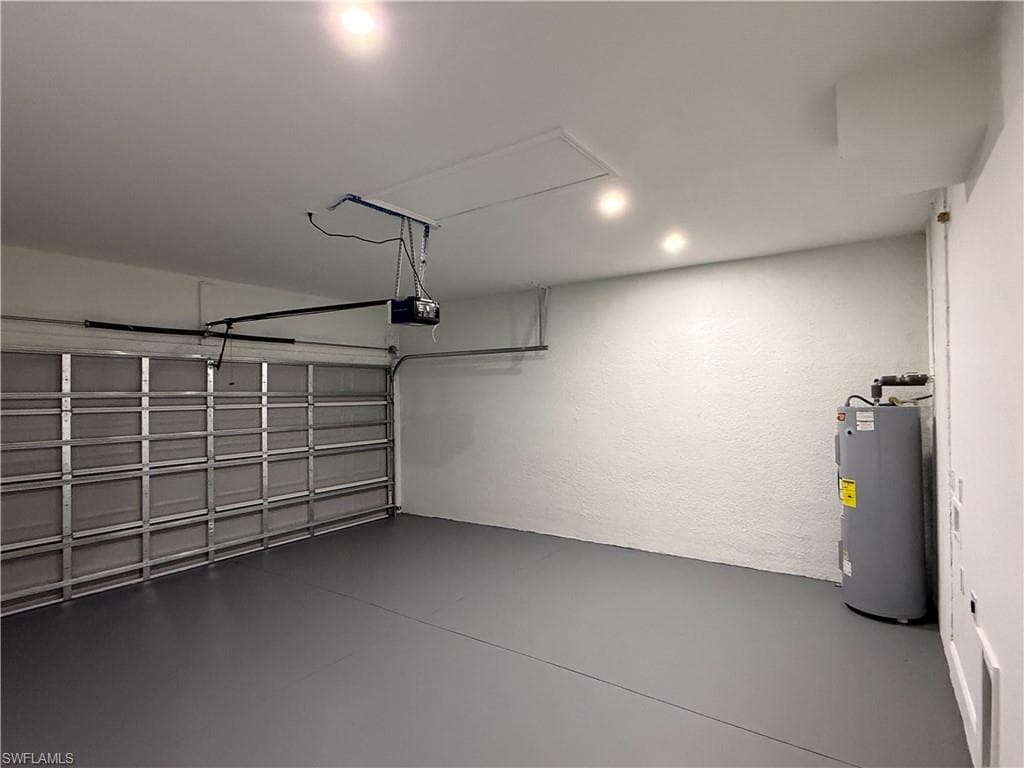 Garage featuring water heater, a textured wall, and a garage door opener