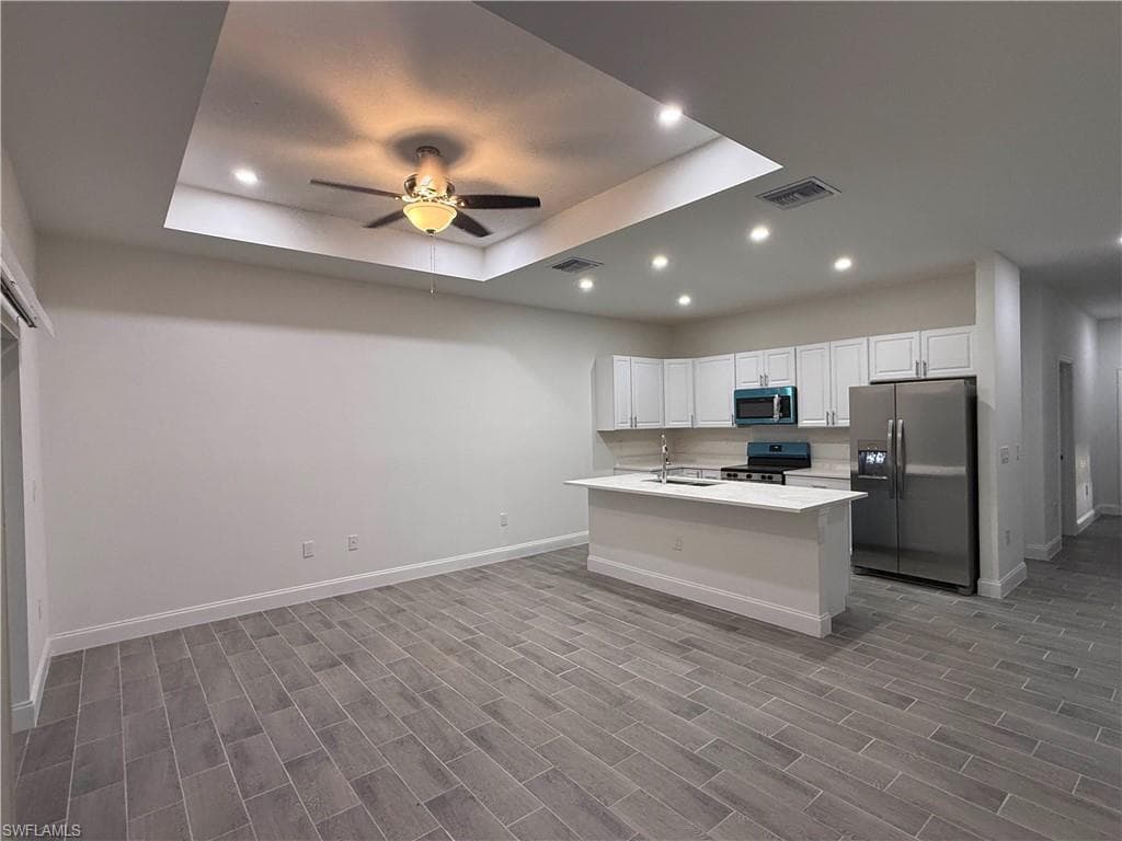Kitchen with a tray ceiling, appliances with stainless steel finishes, recessed lighting, white cabinets, and open floor plan