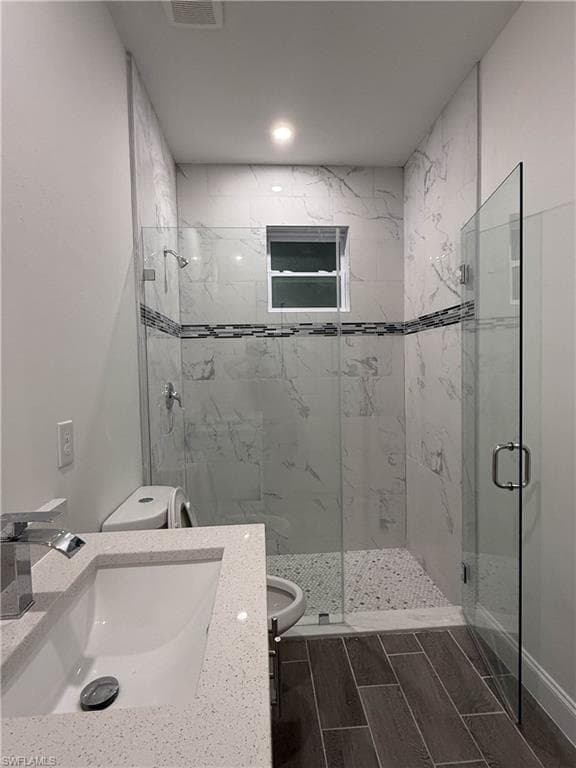 Bathroom with a marble finish shower, wood tiled floors, and vanity