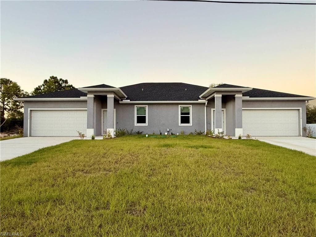 View of front of home with a lawn, stucco siding, driveway, and an attached garage