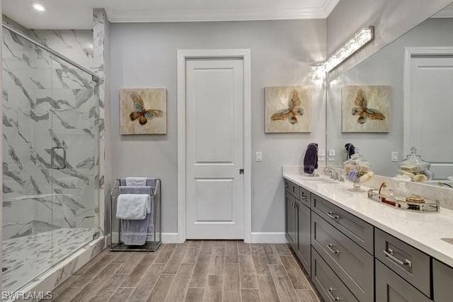 Featuring a frameless glass enclosed frameless shower, porcelain tiled flooring, vanity with dual sinks, and quartz countertopsvanity, porcelain tile plank wood like floor, crown molding and walk-in-closet