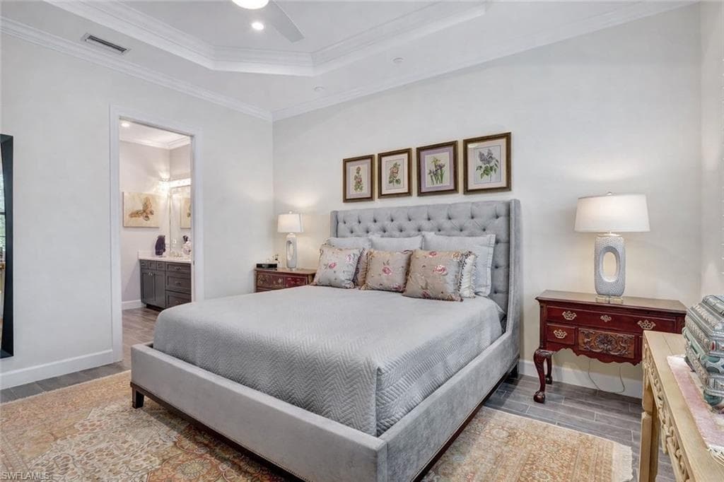 Primary Bedroom with porcelain wood-like floors, a ceiling fan, crown molding, a raised ceiling, and primary bathroom