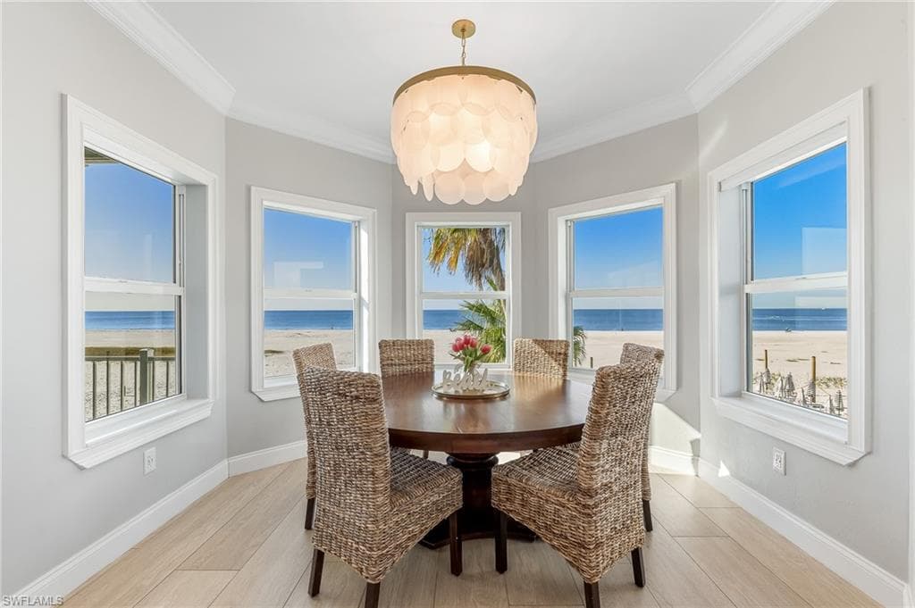 Dining room with ornamental molding, view of water and beach, light wood-style floors, and a chandelier