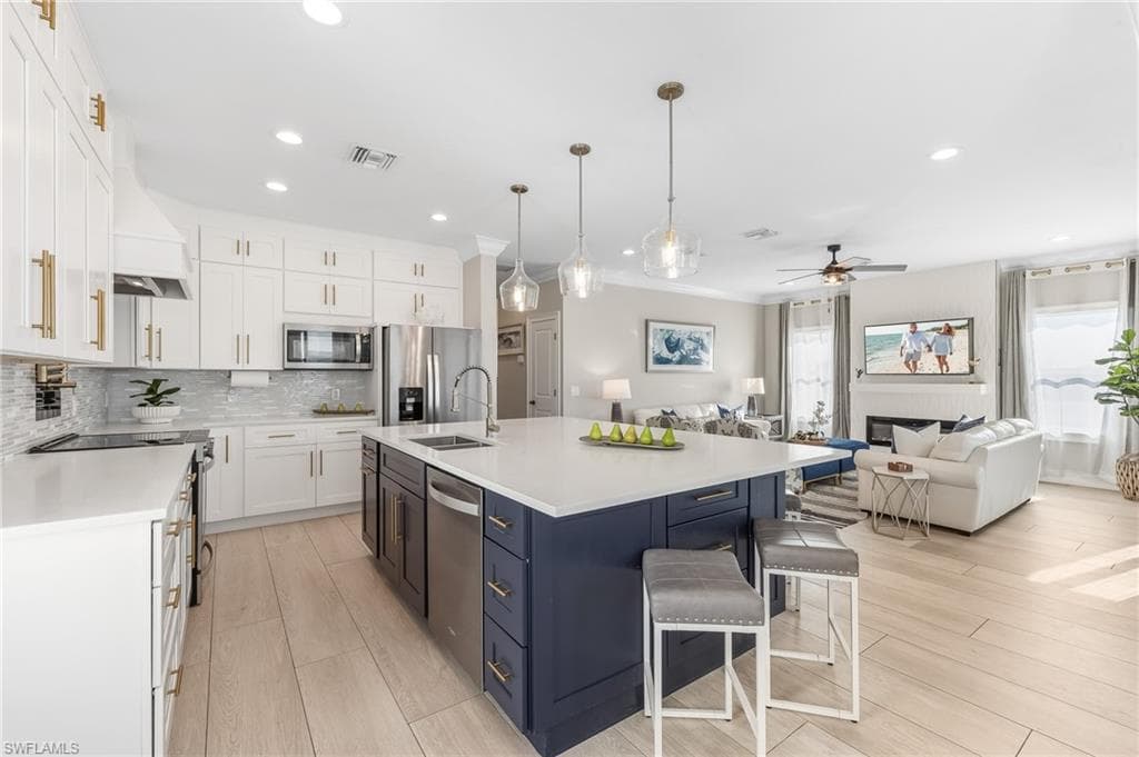 Kitchen with white cabinetry, open floor plan, hanging light fixtures, an island with sink, and backsplash