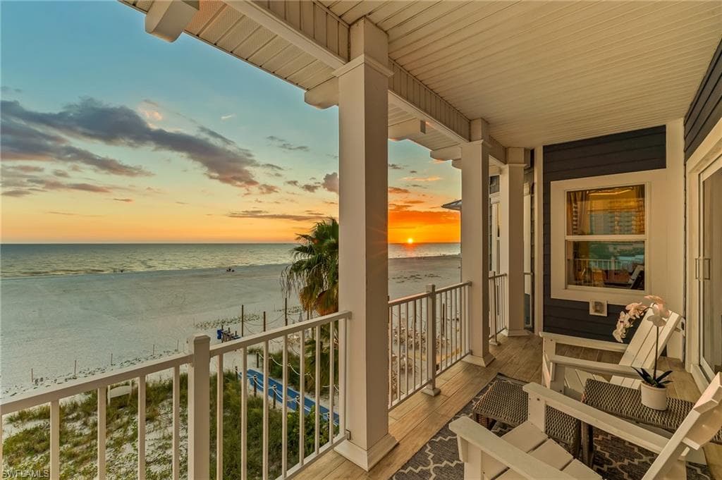Balcony featuring view of water and beach and a sunroom
