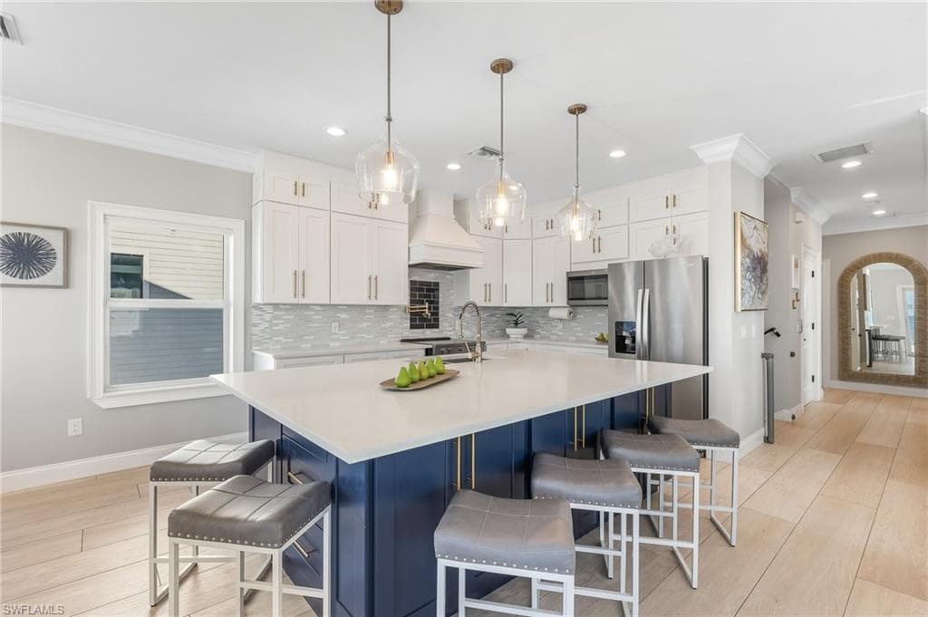 Kitchen with ornamental molding, white cabinets, a kitchen bar, decorative light fixtures, and a center island with sink