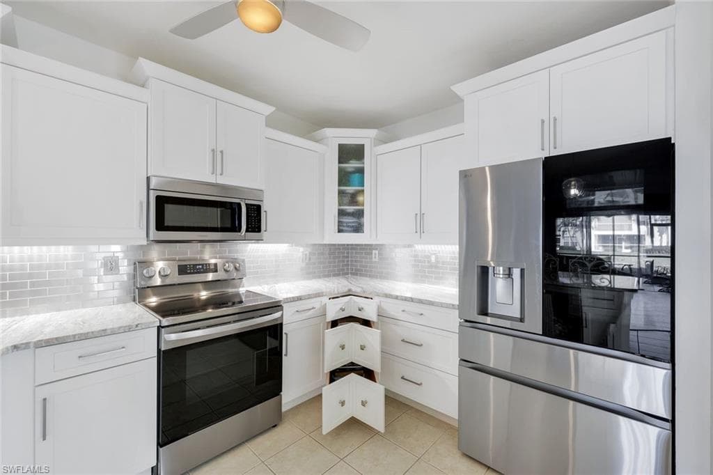 Kitchen with appliances with stainless steel finishes, white cabinets, glass insert cabinets, and light stone countertops
