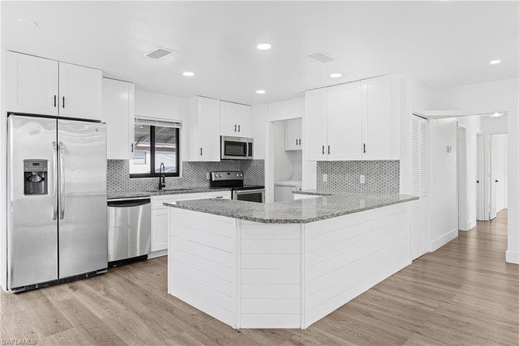 Kitchen featuring light stone countertops, appliances with stainless steel finishes, a peninsula, white cabinets, and light wood-style flooring