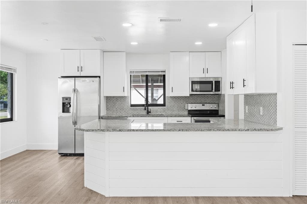 Kitchen with light stone countertops, white cabinetry, a peninsula, appliances with stainless steel finishes, and light wood-style flooring