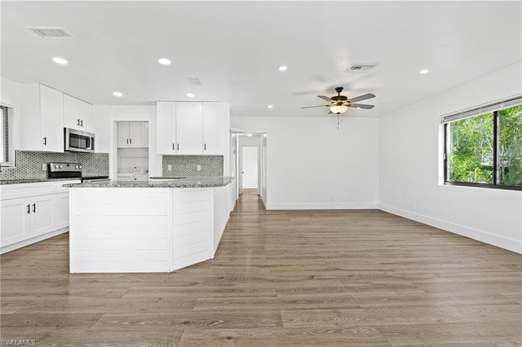 Kitchen featuring backsplash, white cabinets, light stone counters, recessed lighting, and a peninsula