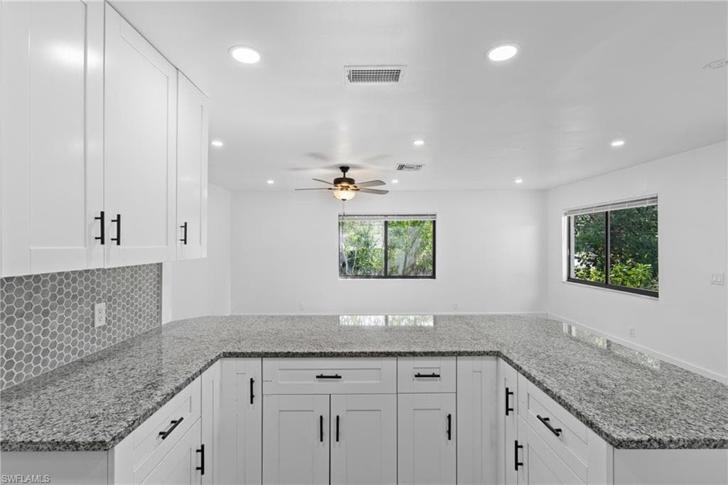 Kitchen featuring light stone counters, a peninsula, backsplash, white cabinets, and recessed lighting