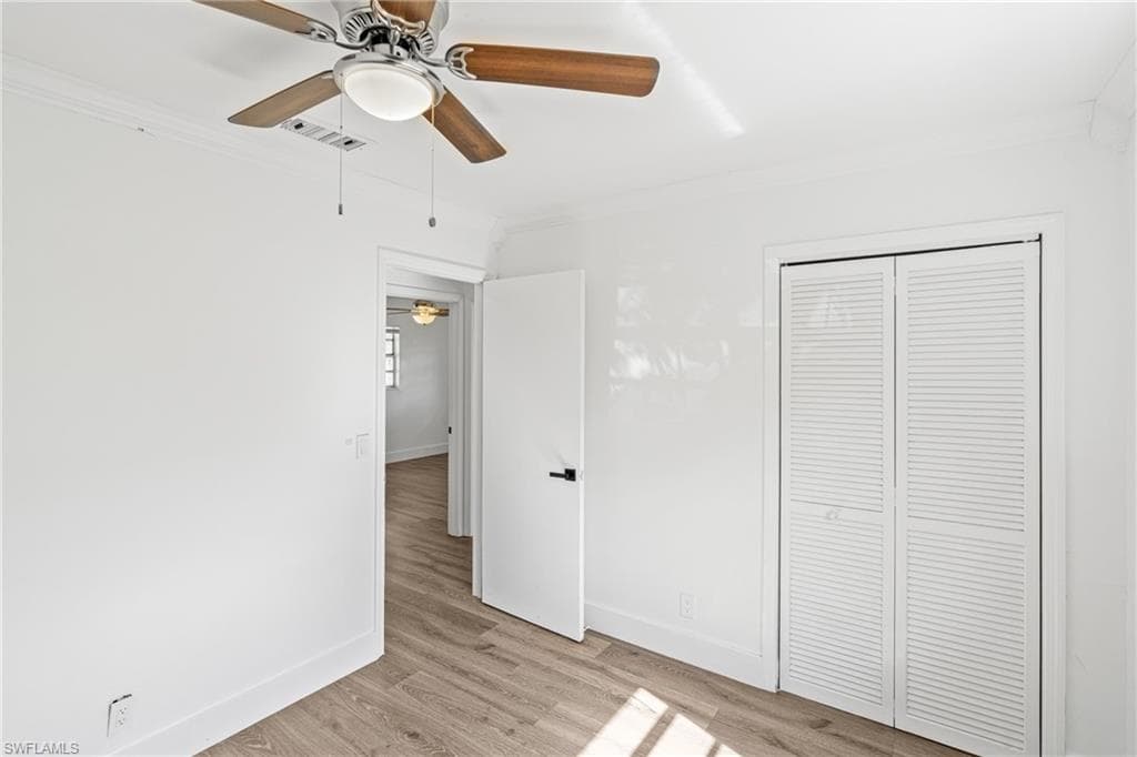 Unfurnished bedroom featuring ornamental molding, light wood-style flooring, a ceiling fan, and a closet