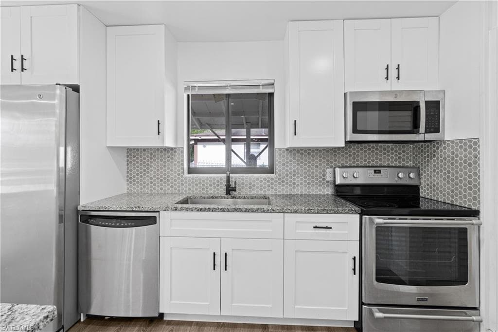 Kitchen featuring stainless steel appliances, light stone countertops, white cabinets, tasteful backsplash, and light wood-type flooring