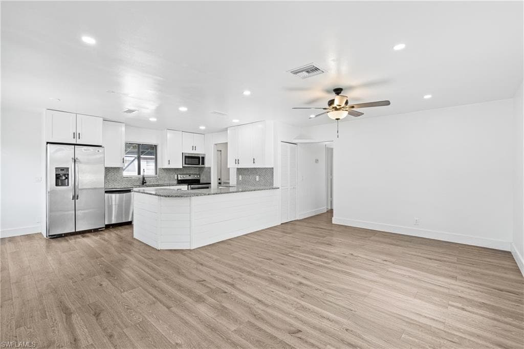 Kitchen featuring stainless steel appliances, white cabinets, light wood-style floors, tasteful backsplash, and a peninsula