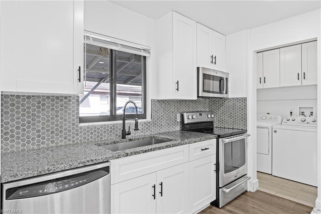 Kitchen featuring stainless steel appliances, washer and dryer, dark stone counters, and light wood finished floors