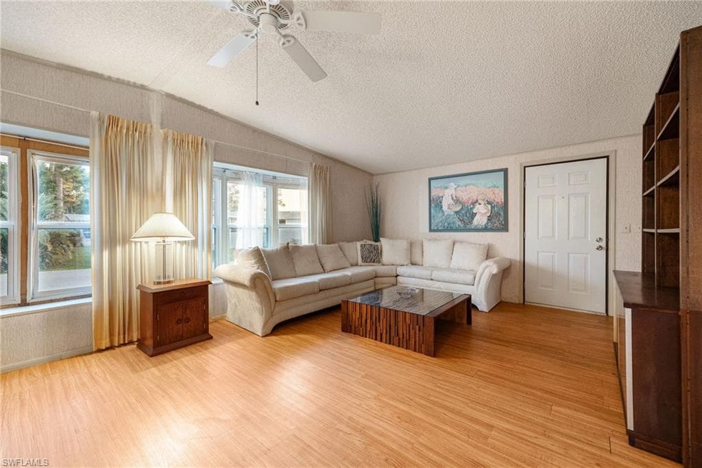 Living room featuring a textured ceiling, light wood-style floors, lofted ceiling, radiator, and a ceiling fan