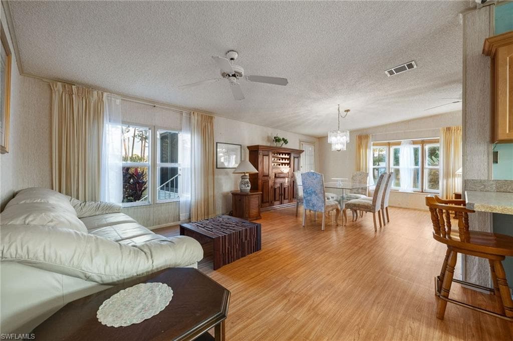 Living area featuring light wood-style flooring, a textured ceiling, a ceiling fan, and a chandelier
