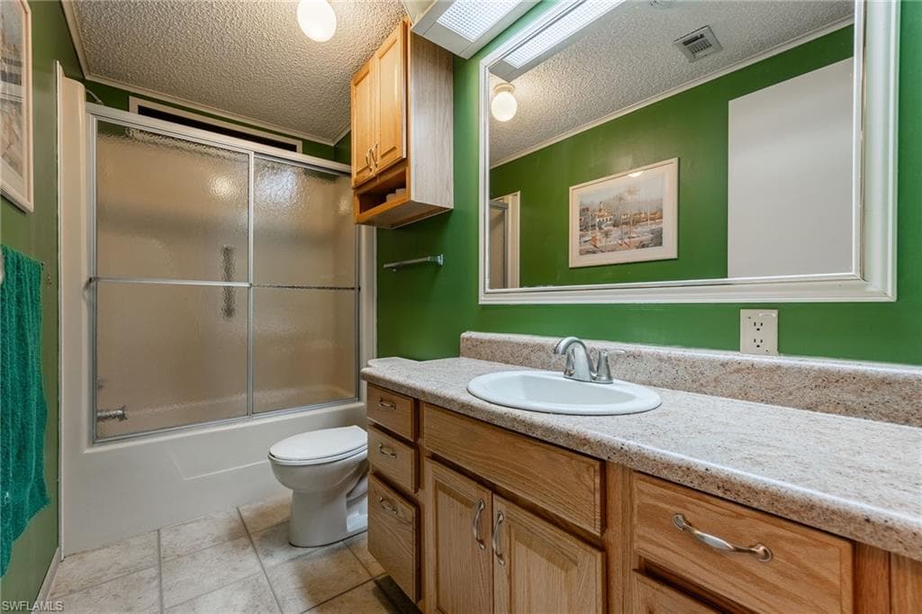 Bathroom featuring vanity, a textured ceiling, shower / bath combination with glass door, and light tile patterned floors